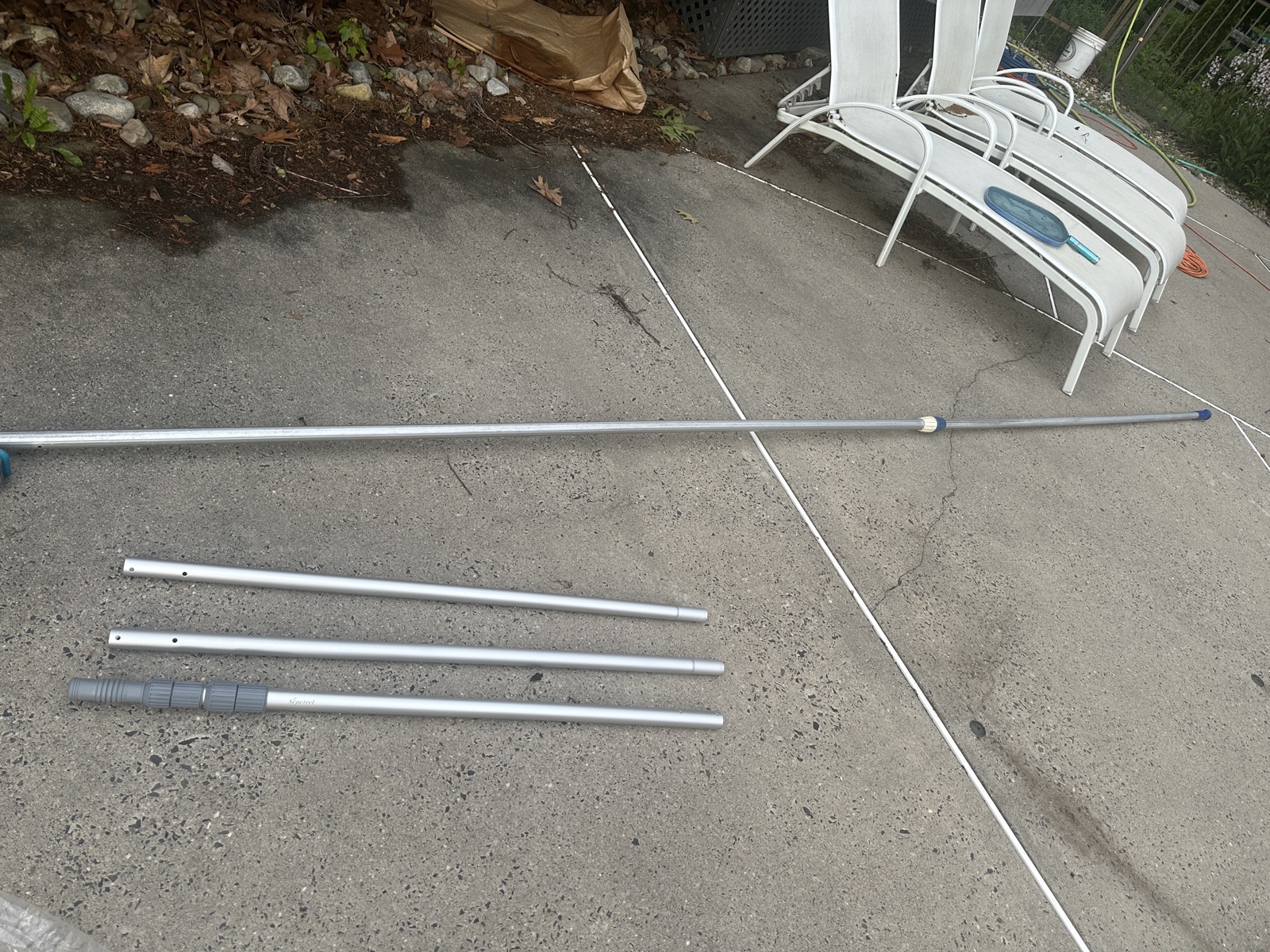 The Sepetrel pool pole fully extended on the driveway, with its three separated sections laid out below it.